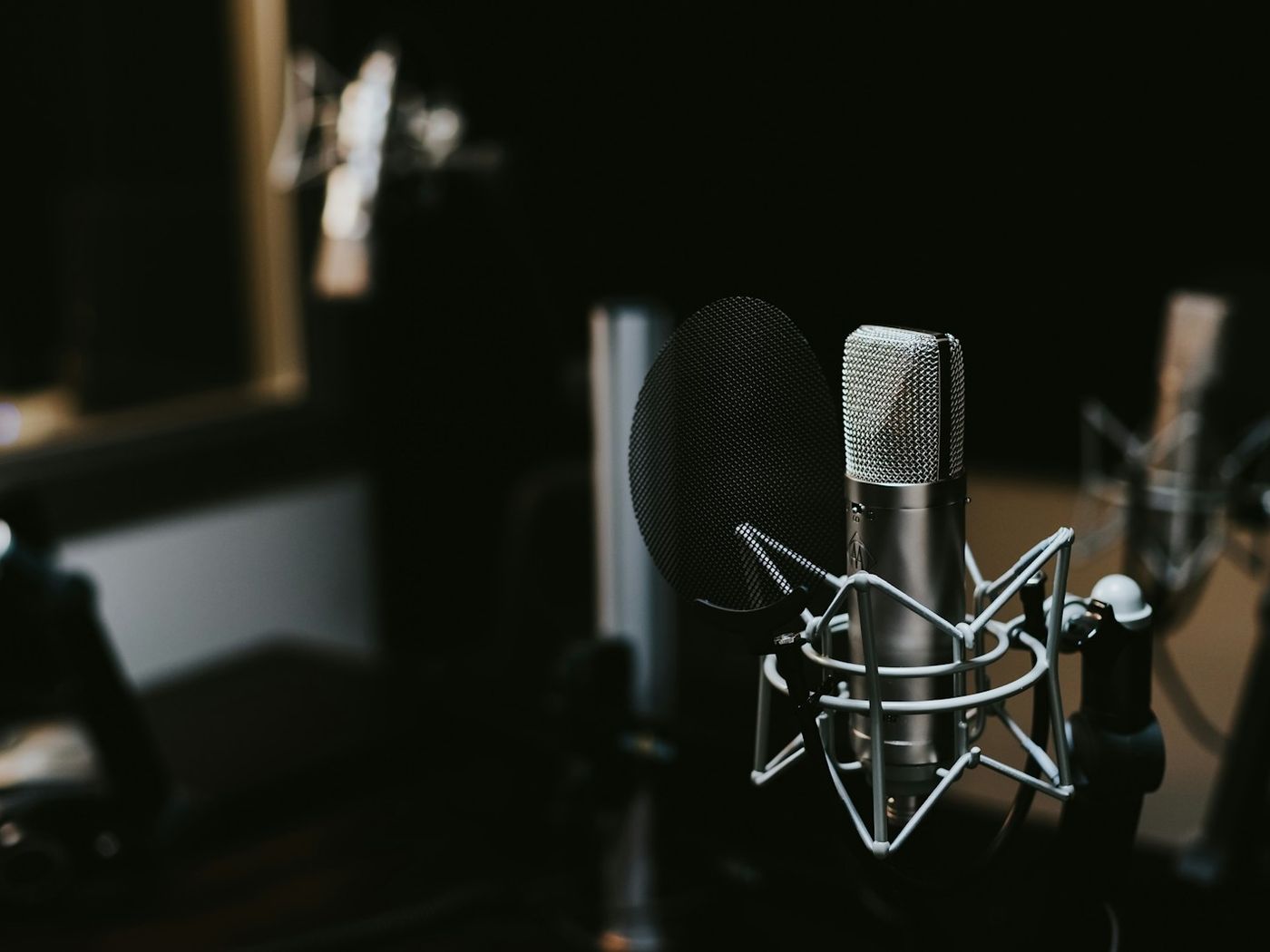 A studio condenser microphone in a shock mount, lit against a dark room