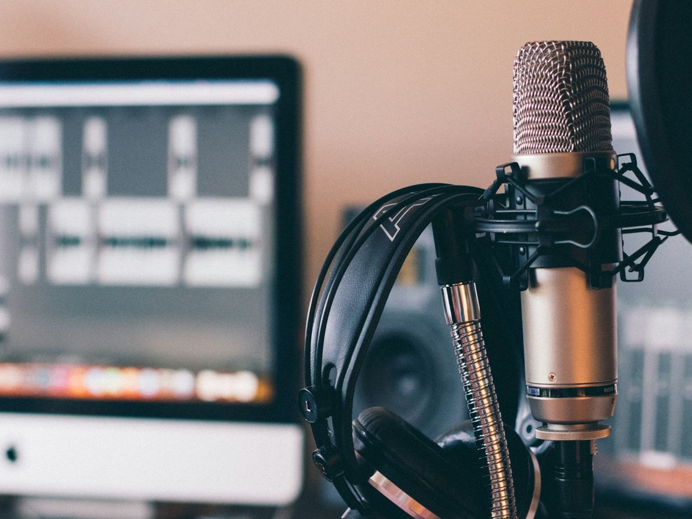 A condenser microphone with headphones hanging beside it and a computer screen behind