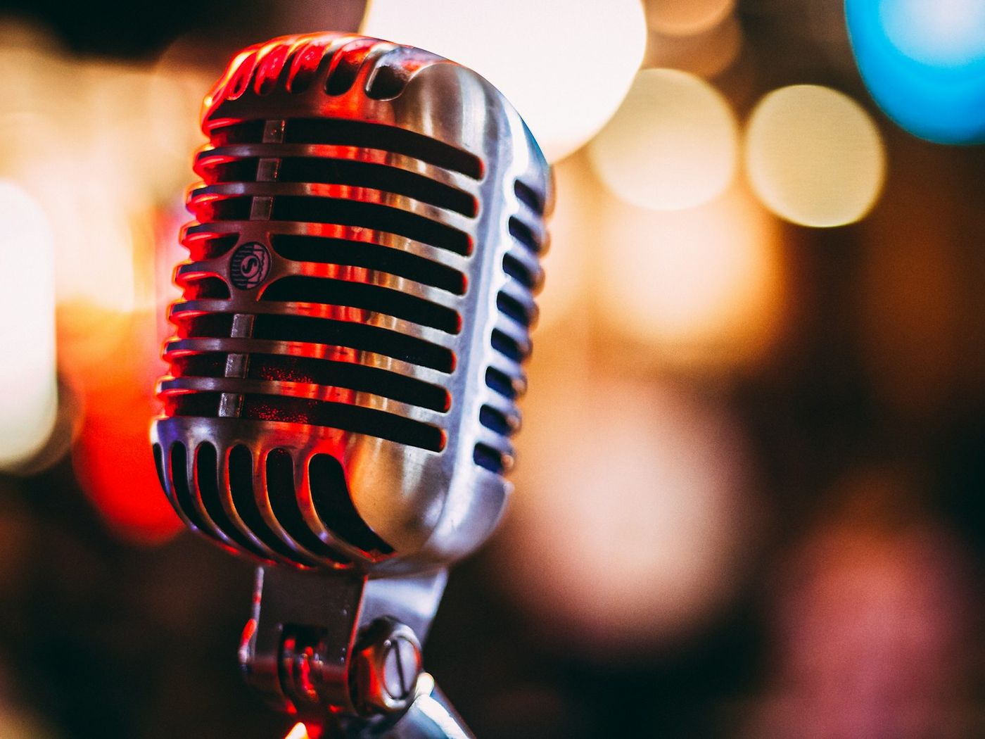 A vintage microphone lit in red against a blurred background of lights