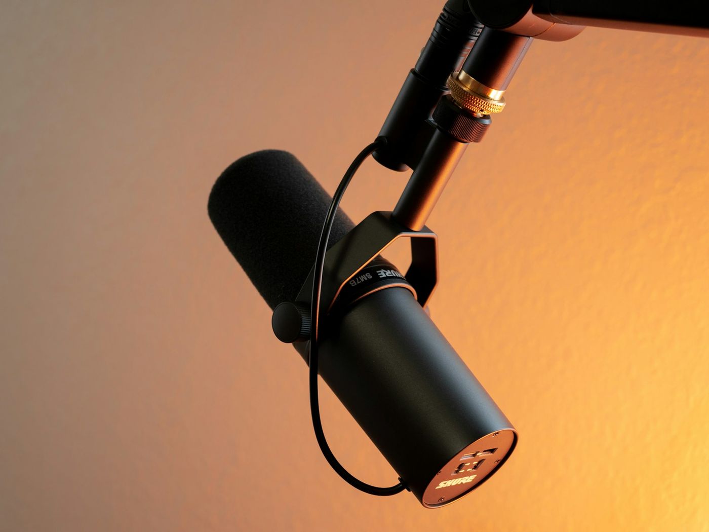 A black broadcast microphone on a boom arm against an orange wall