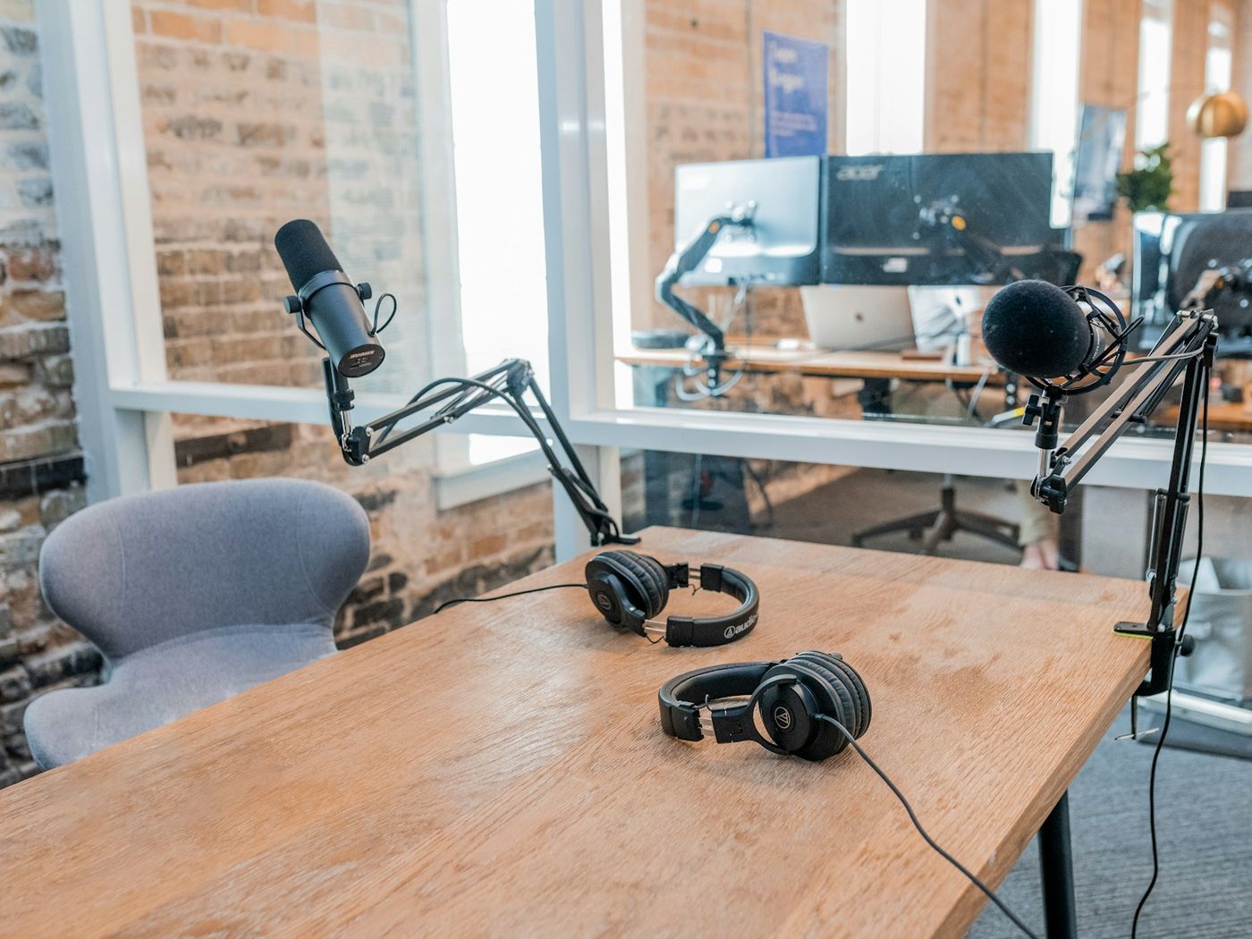 A podcast studio desk with two microphones on boom arms and two pairs of headphones